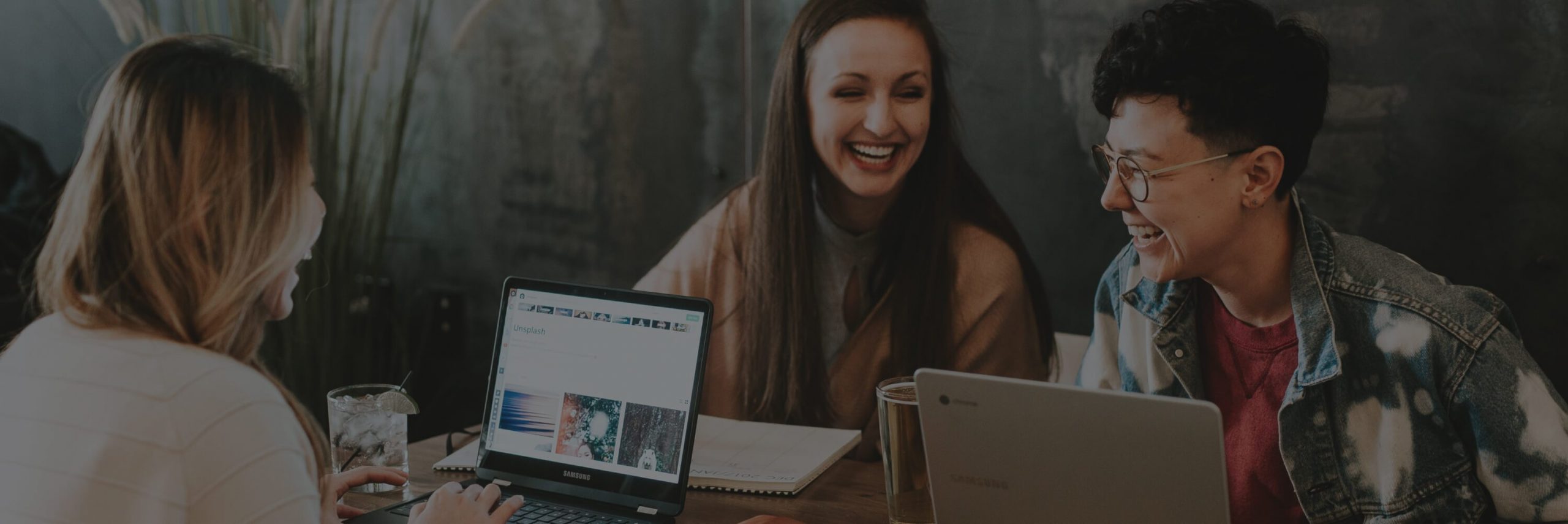 Three friends laughing and working together on laptops.
